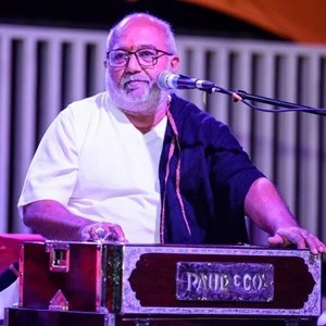 Atul Purohit singing into a microphone behind a harmonium on stage.