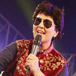 Falguni Pathak performing in sunglasses and an embroidered red jacket, microphone in hand.